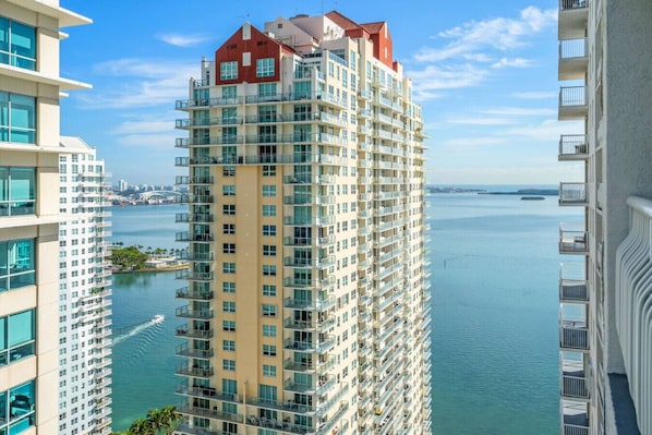 A high-rise hotel with multiple balconies, a view of the water, and a cityscape in the background.