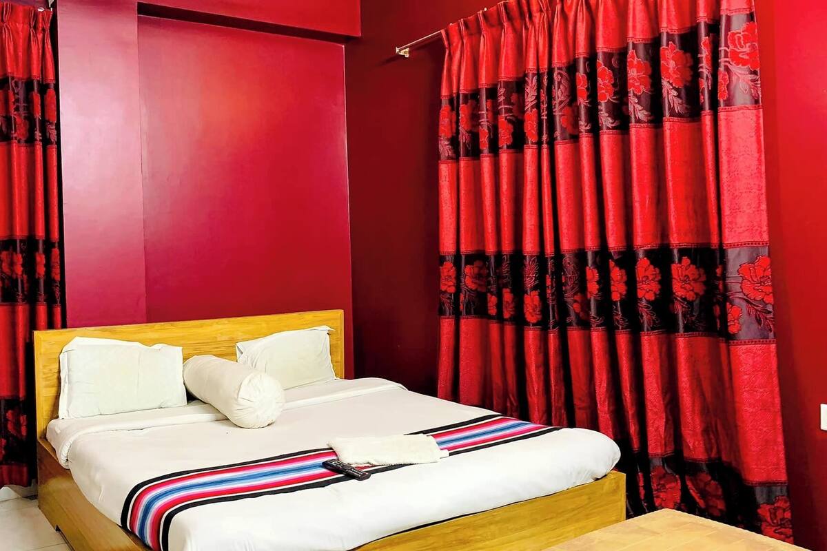 Une chambre à coucher avec un lit en bois, du linge de lit blanc et des rideaux rouges ornés de motifs floraux.