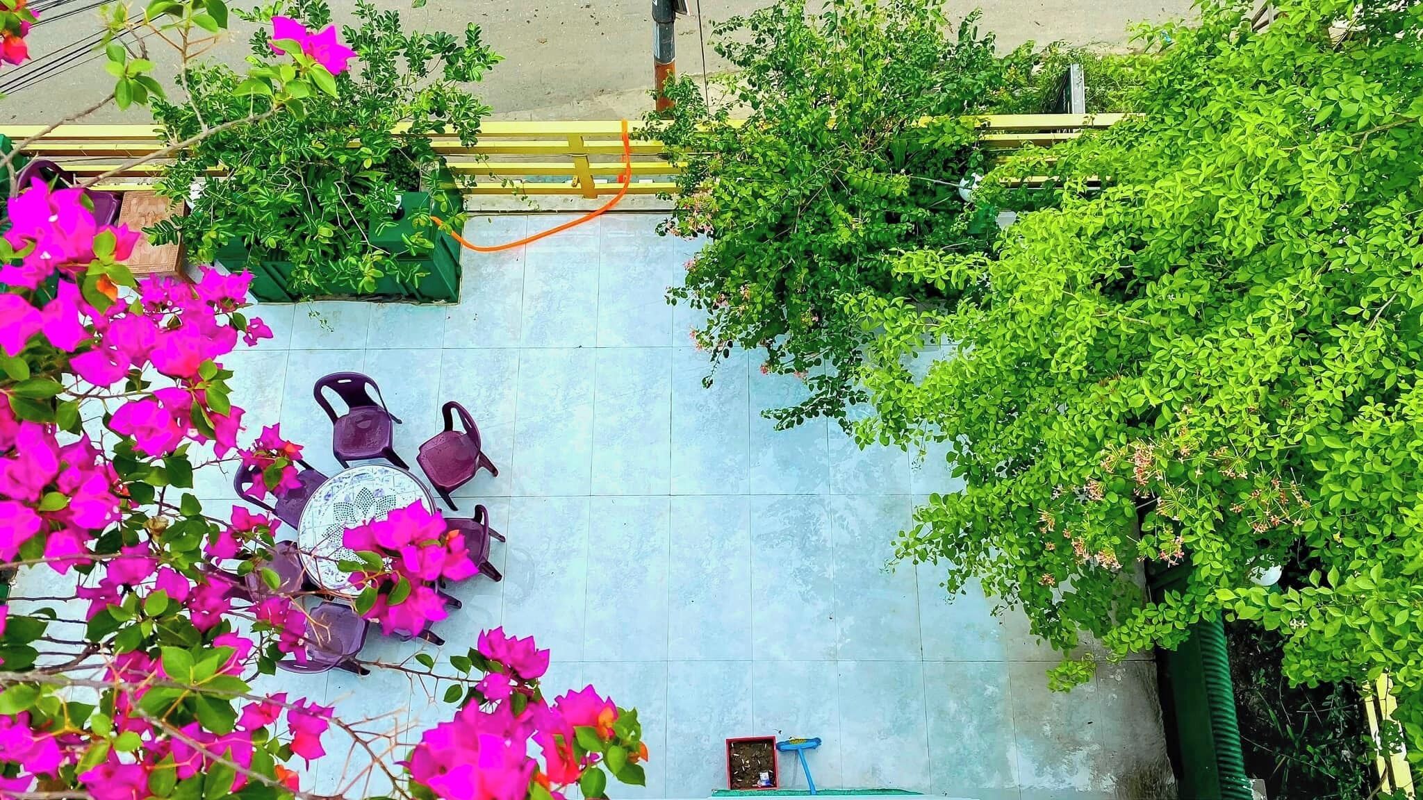 A tiled patio area with a table and chairs, surrounded by greenery and bougainvillea flowers.