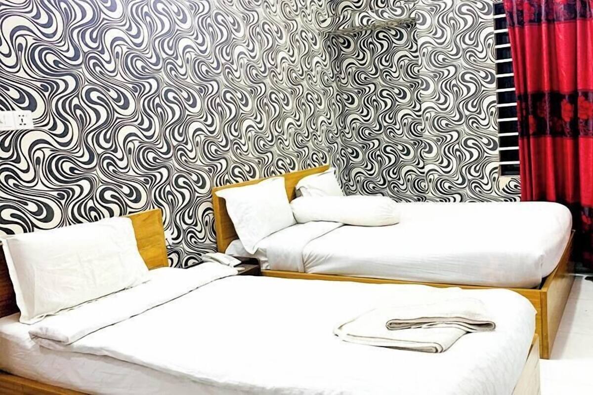 Une chambre d’hôtel avec deux lits, une tête de lit en bois, un rideau rouge et une petite table avec une chaise.
