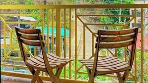 A balcony with two wooden chairs and a small table, overlooking a street with trees and buildings. - Hotel Aranna Residential Bandarban (Bandarban)
