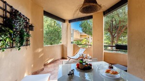 A sunlit balcony with a table set for dining, surrounded by potted plants and a view of buildings and trees. - CT 349 - Stupa Hills - Benalmadena (Benalmádena)