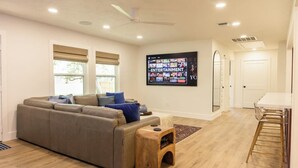 A modern living room with a sofa, a coffee table, and a TV mounted on the wall displaying various channels. - College Station • Pickleball • 2mi Kyle Field (Bryan)