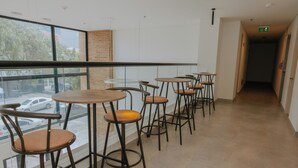 A corridor with round tables and chairs, a glass railing, and a view of parked cars outside.