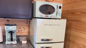Uma cozinha compacta com geladeira antiga, cafeteira e micro-ondas.