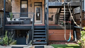 Un edificio de dos pisos con un balcón, asientos al aire libre y una escalera que lleva al piso superior.