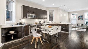 Una cocina moderna con armarios oscuros, una isla central, sillas blancas y una mesa de comedor.