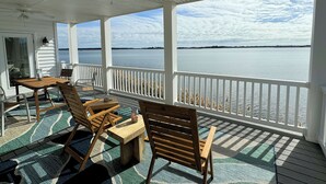 Una terraza techada con vista a un cuerpo de agua tranquilo, mobiliario de madera y un ventilador de techo.