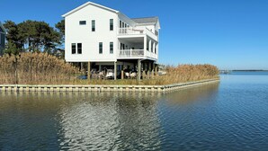 Una casa blanca de dos pisos con balcón, construida sobre pilotes sobre el agua, con un muelle que se adentra en el agua.
