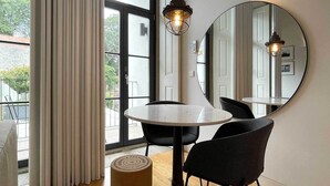 A modern room with a round table, two black chairs, a large mirror, and a hanging light fixture. - Essência Portuense Studios (Porto)