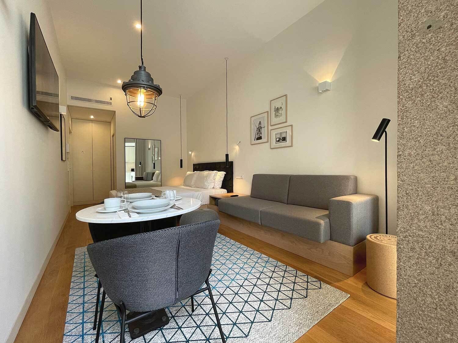 Un salon moderne et bien éclairé, avec une table à manger ronde, un canapé gris et un grand miroir.