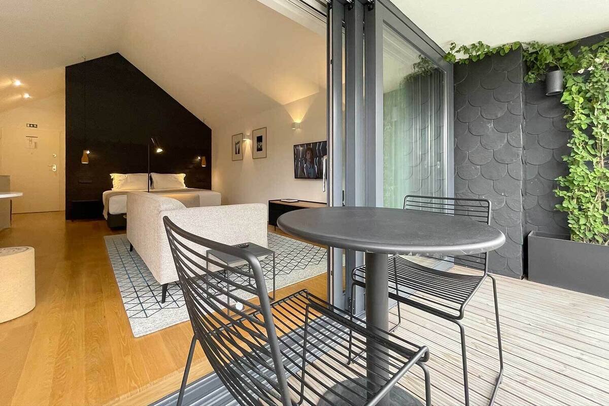 Et moderne hotelværelse med et stort vindue, en balkon med bord og stole, og et hyggeligt opholdsområde med en sofa og sofabord.
