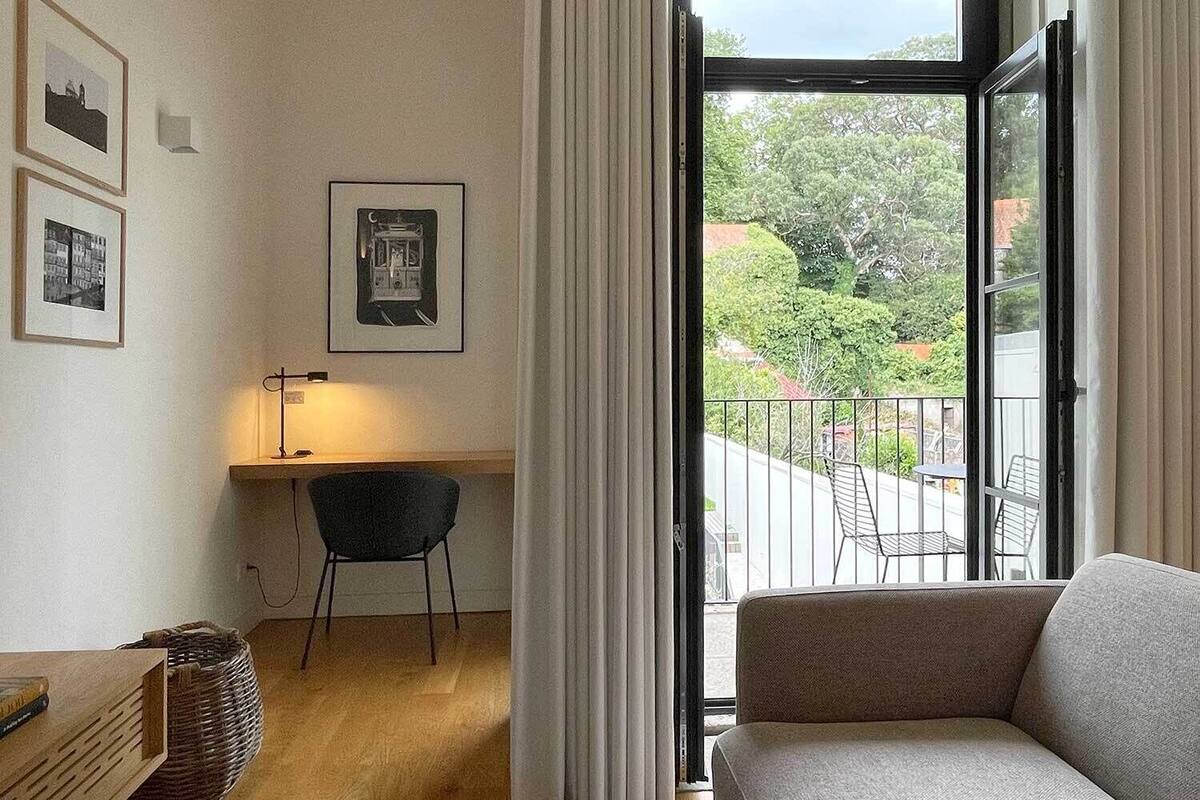 Et værelse med en sofa, et skrivebord med stol, en lampe og billeder i rammer på væggen.