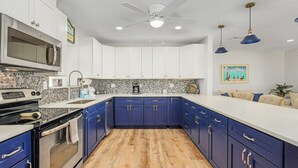 Una cucina moderna con mobili bianchi, dettagli blu, un forno a microonde, un fornello e una ventola a soffitto.