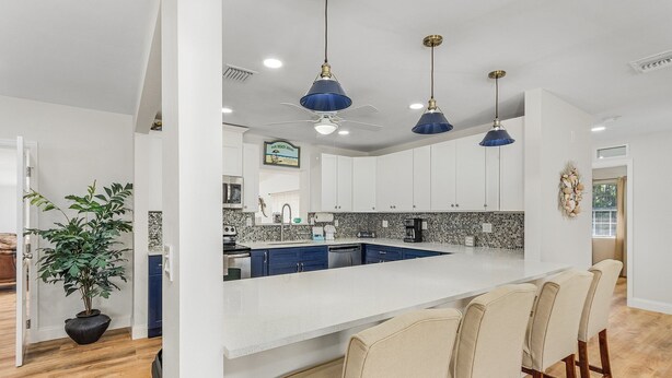 Una cucina moderna con isola centrale, pensili bianchi e lampade a sospensione blu.