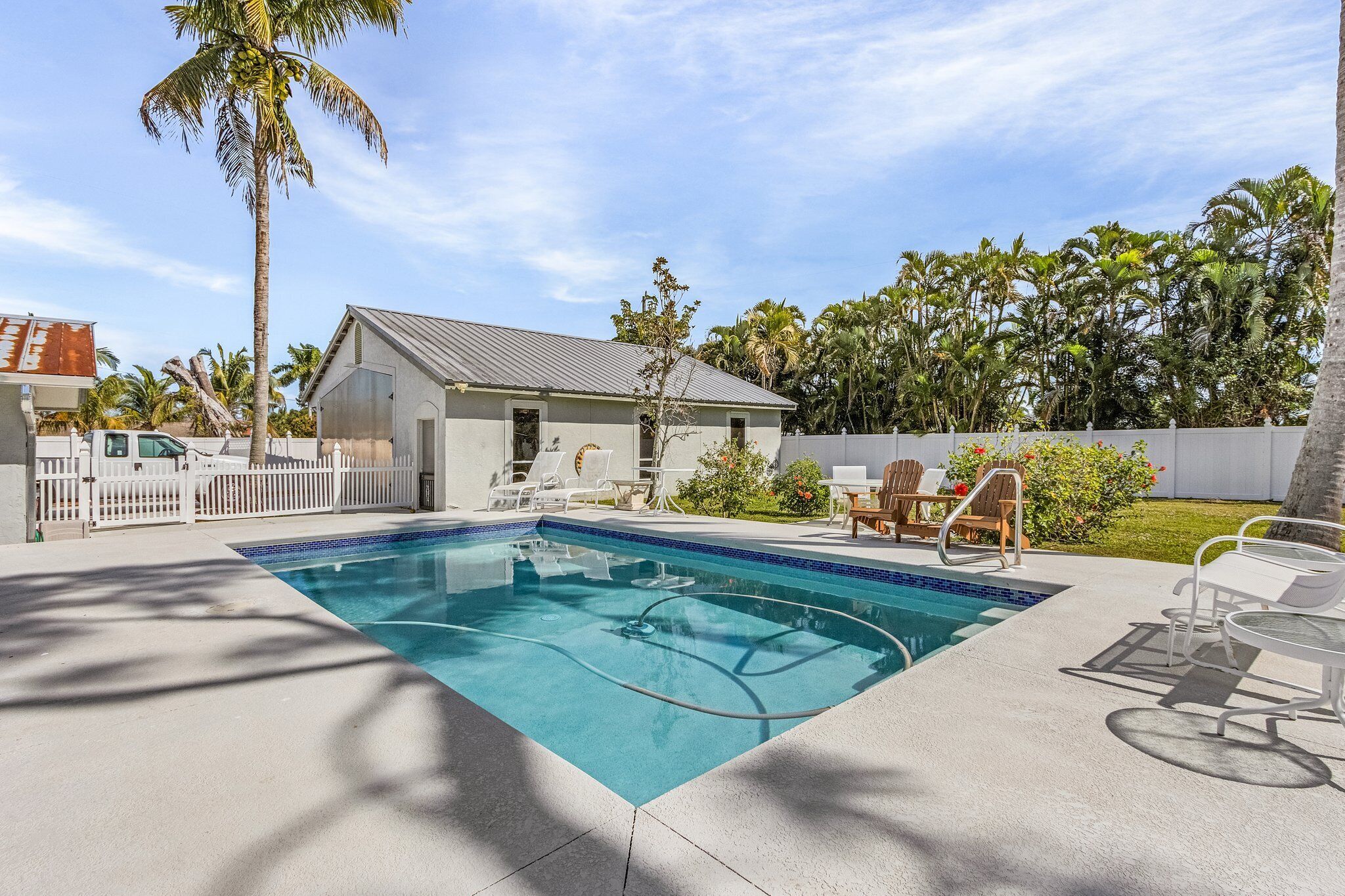 A rectangular swimming pool with a tiled edge, surrounded by a concrete deck. There are lounge chairs and a small table on the deck.