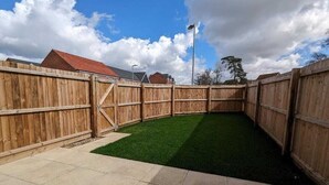 A fenced backyard with artificial grass and a concrete patio. - Watton House | 3 bedroom house with garden | Ipswich, London (Carbrooke)