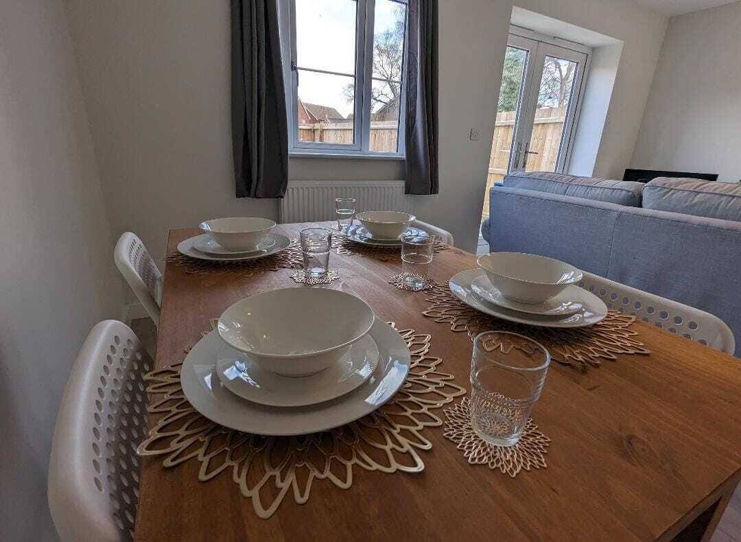 Une table à manger dressée avec des assiettes, des bols et des verres, donnant sur un jardin par une fenêtre.
