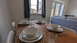 A dining table set with plates, bowls, and glasses, with a view of a backyard through a window. - Watton House | 3 bedroom house with garden | Ipswich, London (Carbrooke)