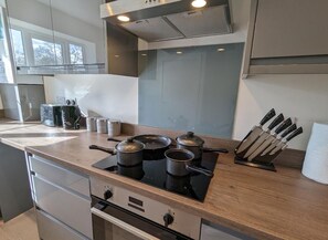 Une cuisine moderne équipée d’une cuisinière à gaz, de casseroles, d’un bloc à couteaux et d’une fenêtre.