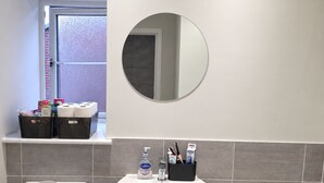 Een badkamer met toilet, wastafel en bad. Boven de wastafel hangt een spiegel en er is een raam met uitzicht op buiten.