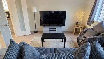 A living room with a sofa, a television on a stand, a floor lamp, and a window with curtains.