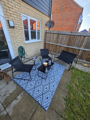 Eine Terrasse mit einem gemusterten Teppich, zwei schwarzen Stühlen, einem kleinen Tisch und einer Kerze.