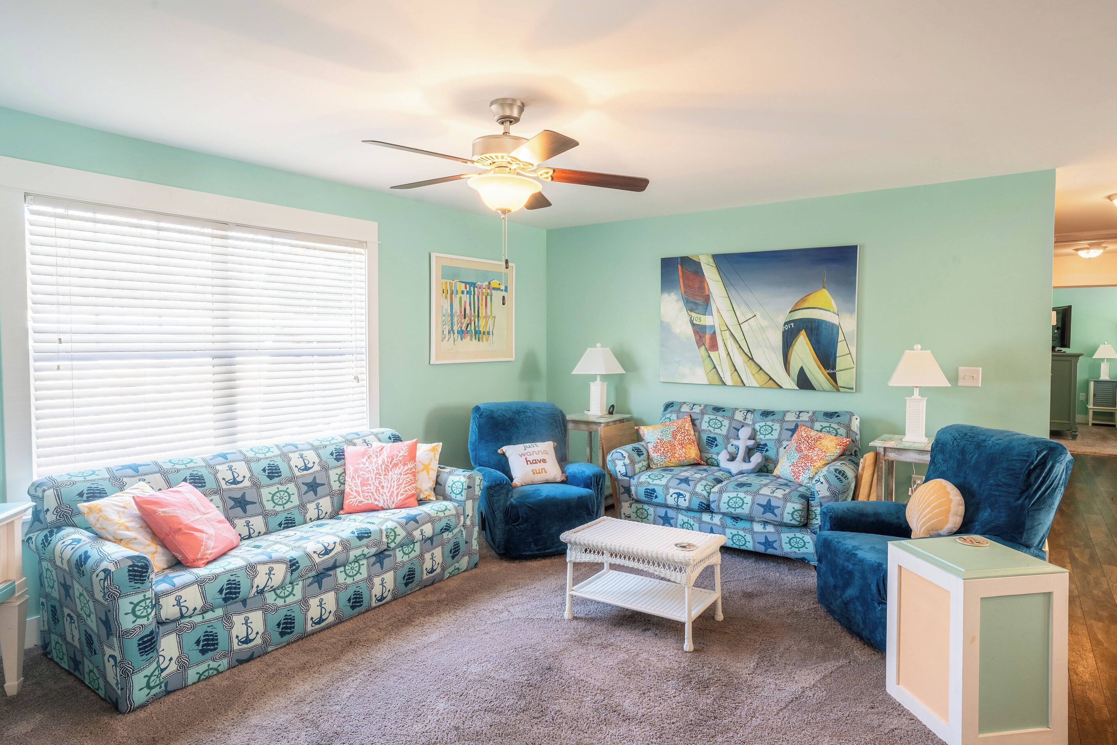 A living room with teal walls, a ceiling fan, and two sofas with nautical patterns.