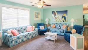 Un salon aux murs de couleur turquoise, doté d’un ventilateur de plafond et de deux canapés aux motifs marins.