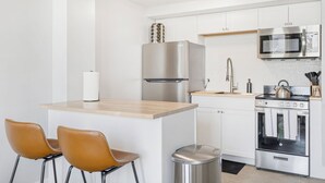 A modern kitchen with stainless steel appliances, a wooden island, and two leather chairs.