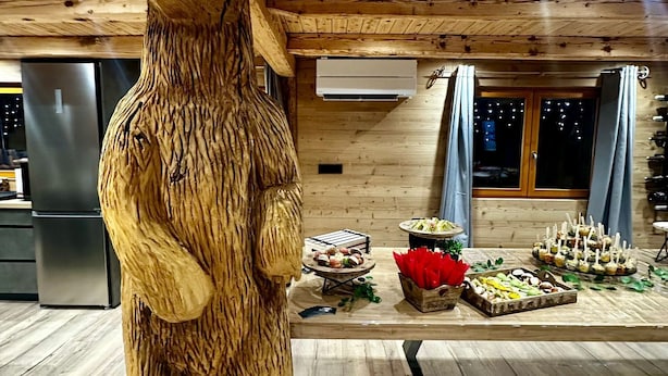 A wooden bear sculpture in a cabin-style room with a wooden ceiling, a refrigerator, and a table with food items.