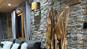 A modern living room with a stone wall, a black leather sofa, and a unique wooden sculpture.