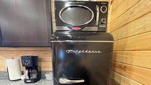 A black Frigidaire refrigerator with a built-in microwave on top, a coffee maker on the counter, and wooden paneling on the walls.