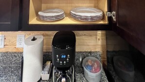A kitchen cabinet with shelves holding white bowls, cups, and plates.