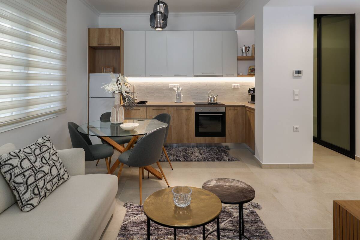 A modern kitchen with wooden cabinets, a dining area with a glass table and chairs, and a living room with a sofa and coffee table.