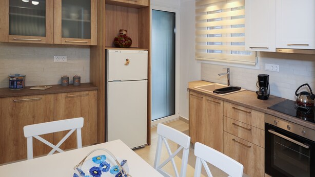 A modern kitchen with wooden cabinets, a white refrigerator, a coffee maker, and a kettle. - Fili's Central Spots (Volos)