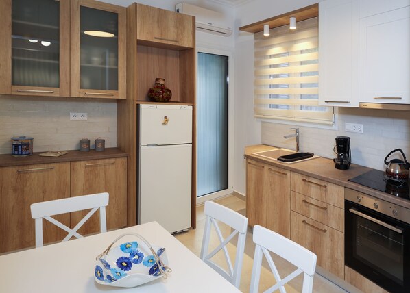 A modern kitchen with wooden cabinets, a white refrigerator, a coffee maker, and a kettle. - Fili's Central Spots (Volos)
