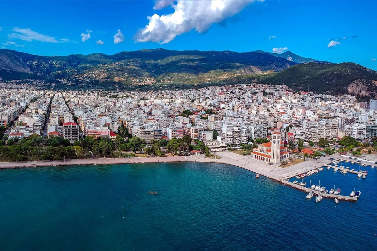 A coastal cityscape with dense urban development, a prominent church with a bell tower, and a marina with boats.