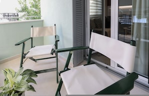 A balcony with two green chairs and a potted plant.