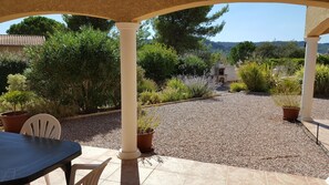Un espace extérieur abrité, aménagé avec une table et des chaises, entouré de gravier et de plantes en pot.