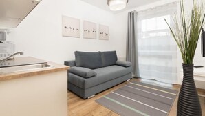 Una sala de estar moderna con un sofá gris, una zona de cocina con un lavamanos y un ventanal con cortinas.