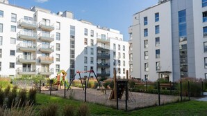 Un edificio residencial con varios balcones, un parque infantil y un jardín vallado.