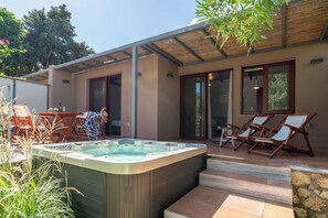 Ein moderner Außenbereich mit Whirlpool, der von Stufen erreichbar ist, umgeben von Holzliegen und einer überdachten Lounge-Ecke.