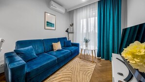 A modern living room with a blue sofa, a small round table, and a potted plant. - Warsaw Airport Apt- Parking&Terrace - by Rentujemy (Warszawa)