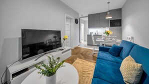 A modern living room with a flat-screen TV, a blue sofa, and a small white table with a plant. - Warsaw Airport Apt- Parking&Terrace - by Rentujemy (Warszawa)
