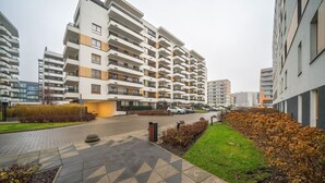 A modern apartment complex with multiple floors, a paved courtyard, and a landscaped area with shrubs and a small garden. - Warsaw Airport Apt- Parking&Terrace - by Rentujemy (Warszawa)
