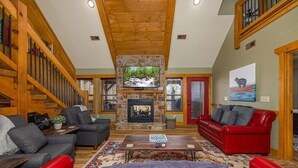 A spacious living room with a stone fireplace, a red couch, and a television mounted above it. - Luna Bear Lodge (Gatlinburg)