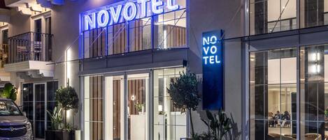 Ett hotell med en tydlig skylt som visar texten ”NOVOTEL”, stora glasfönster och en modern fasad.