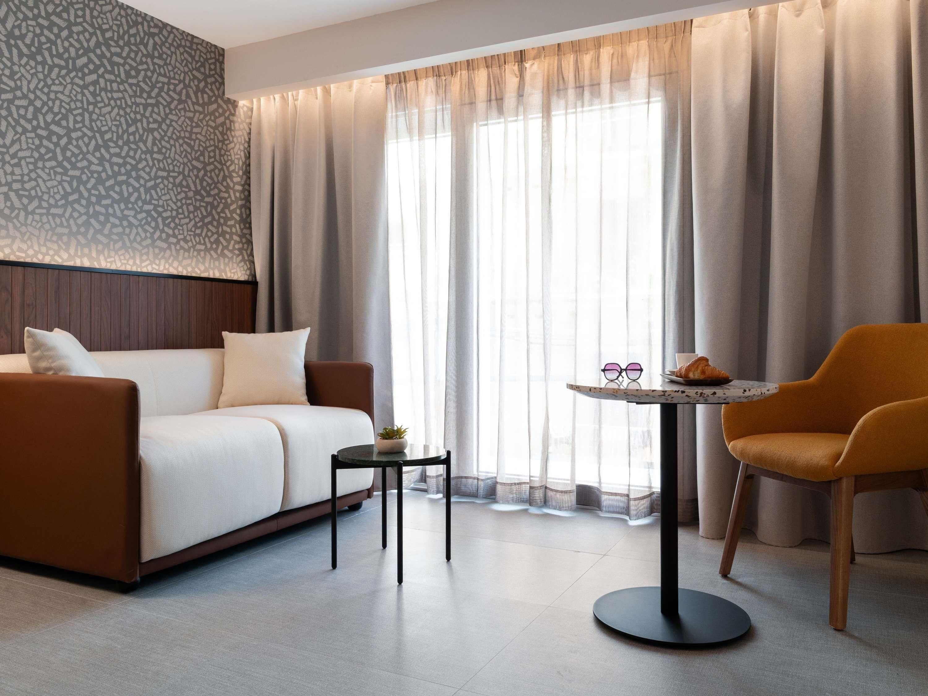 A modern hotel room with a sofa, a round table with a croissant, and a chair.