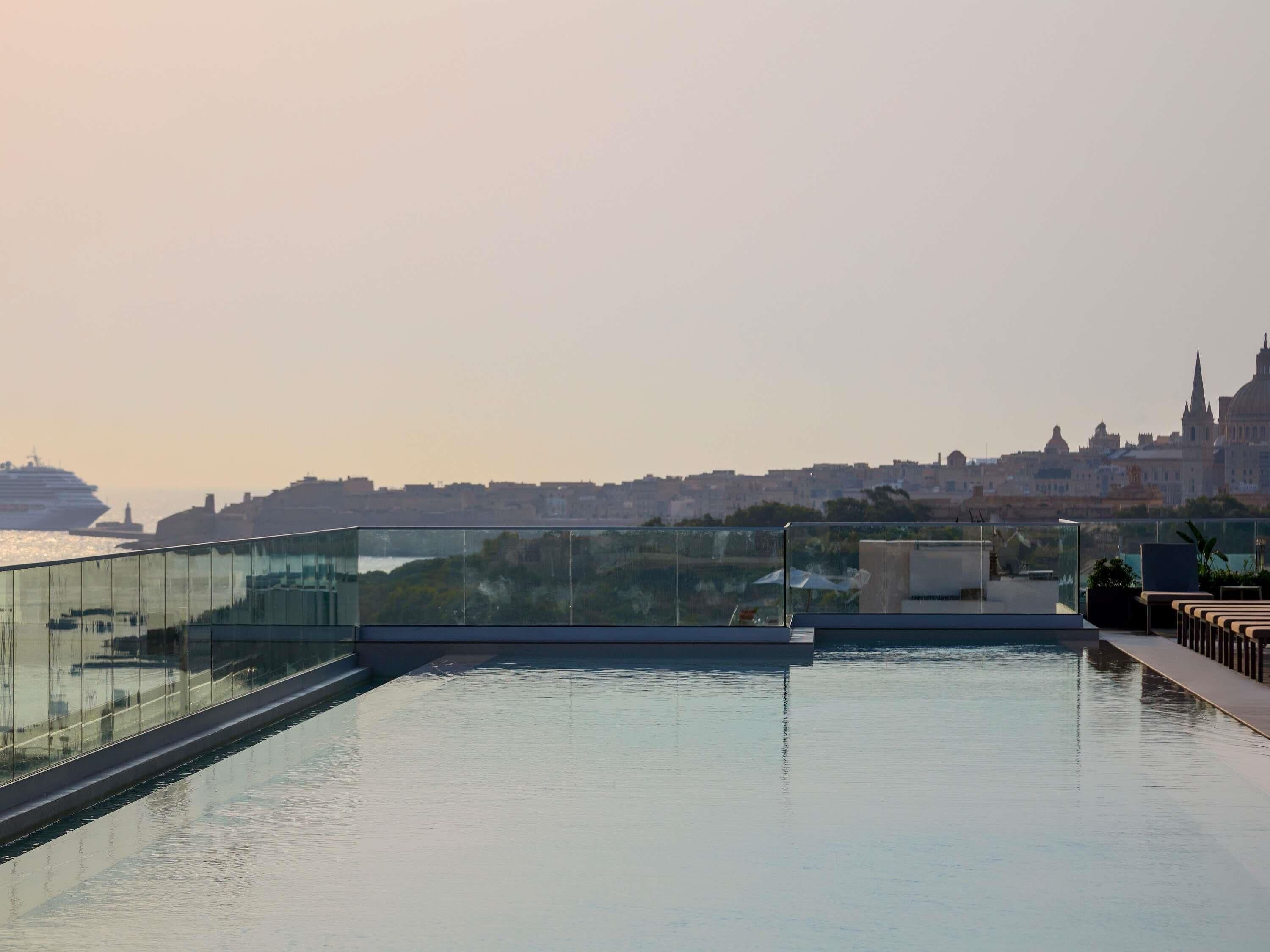 A rooftop pool with a glass barrier, overlooking a cityscape with a prominent cathedral.